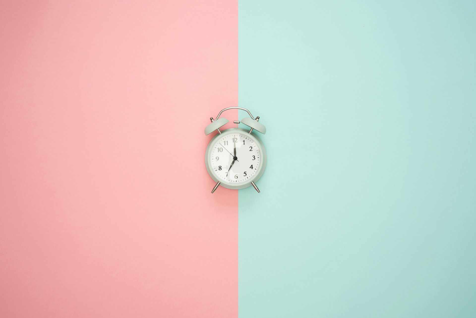 An alarm clock is sitting on a pink and blue background.