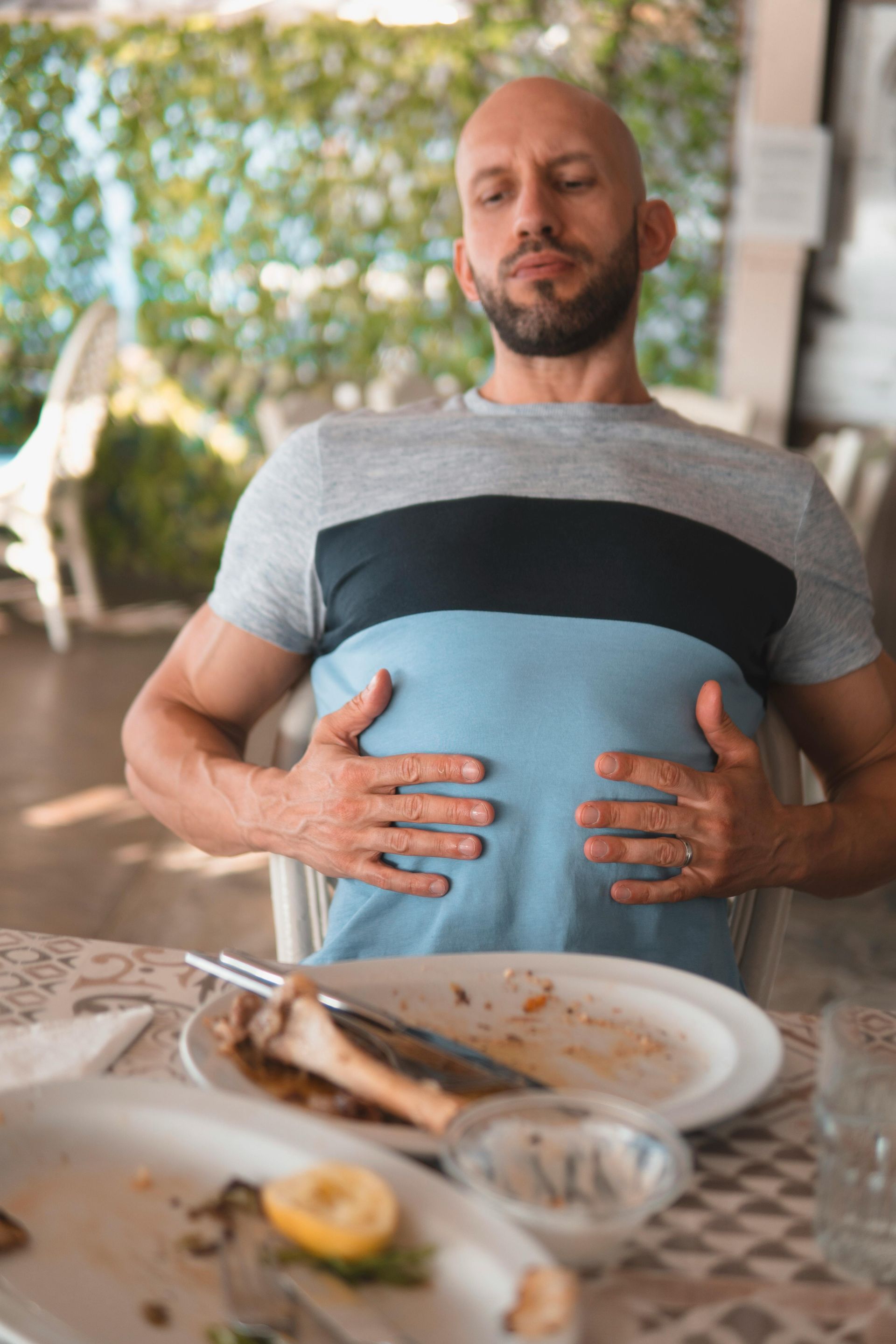 A man is sitting at a table with his hands on his stomach.