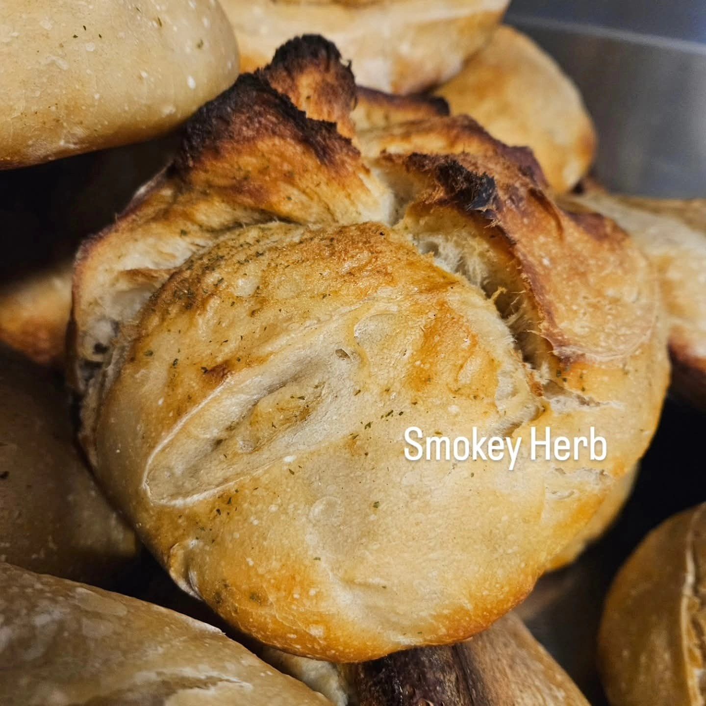 A golden-brown, rustic-style artisan bread roll with herbs, labeled 