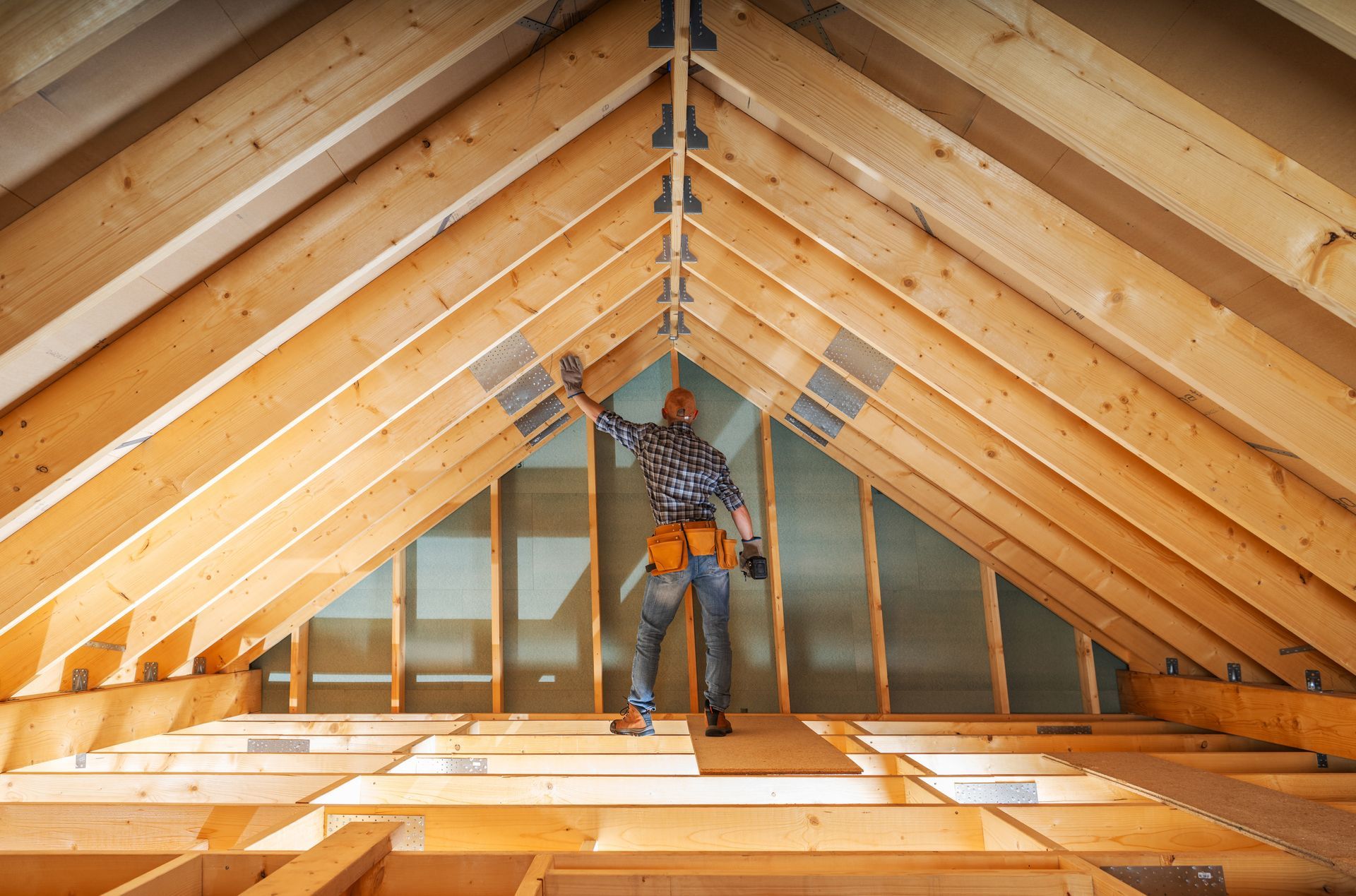 A person working in an attic, with wooden beams and a partially framed ceiling.
