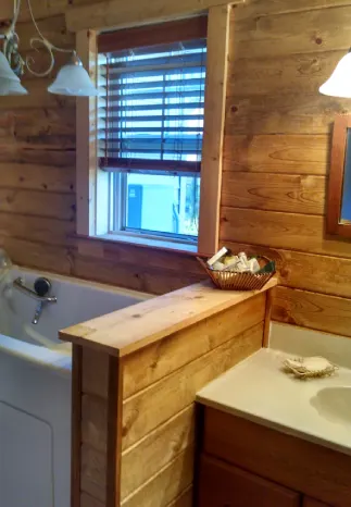 Bathroom with wood-paneled walls, a window with blinds, a bathtub, and a sink.