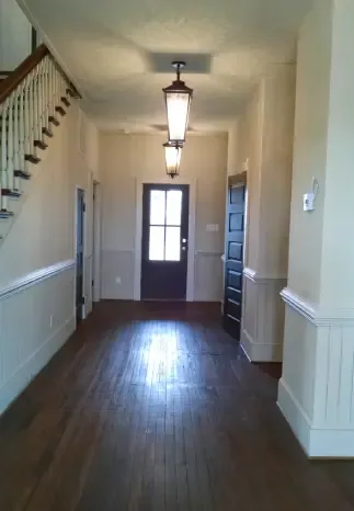 Hallway with wood floors, stairs, and dark doors, with hanging lights and wainscoting.