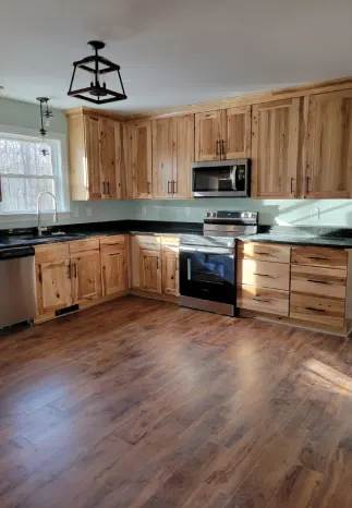 Kitchen with light wood cabinets, dark countertops, stainless steel appliances, and brown flooring.