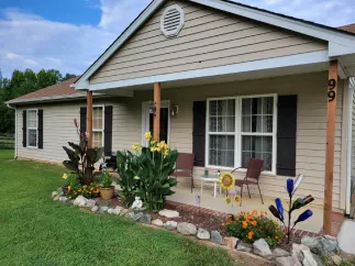 Tan house with porch and landscaping. Features include flowers, rocks, and a green lawn.