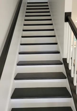 Staircase with black treads and risers painted white, dark railing on the left and white posts with a dark rail on the right.
