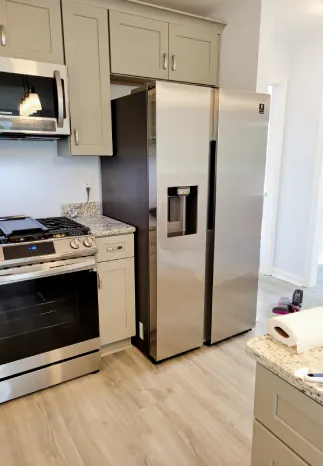 Stainless steel refrigerator in a kitchen with gray cabinets and a stove.