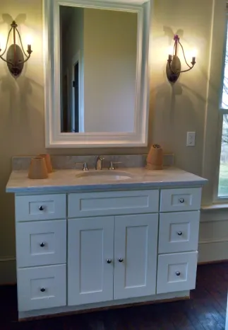 White bathroom vanity with marble countertop, mirror, and sconces.