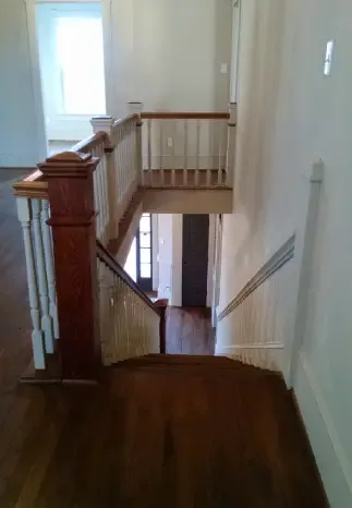 Wooden staircase in a home; view from above. Dark brown wood treads, white railing, and a window in the background.