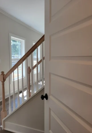 White door partially open, revealing a staircase with a wooden handrail and white balusters.
