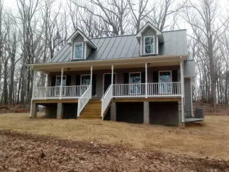 Gray house with metal roof, porch, and two dormers, set in a wooded area.