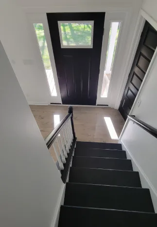 Staircase leading down to an entryway with black door, white trim, and a window above the door.
