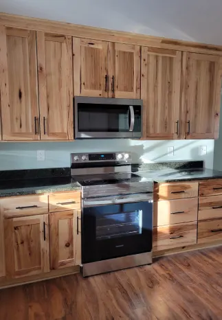 Kitchen with natural wood cabinets, stainless steel appliances, black countertops, and light blue backsplash.