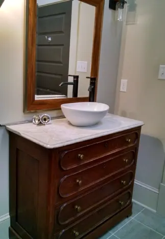 Bathroom with antique dresser vanity, marble top, vessel sink, and large framed mirror.