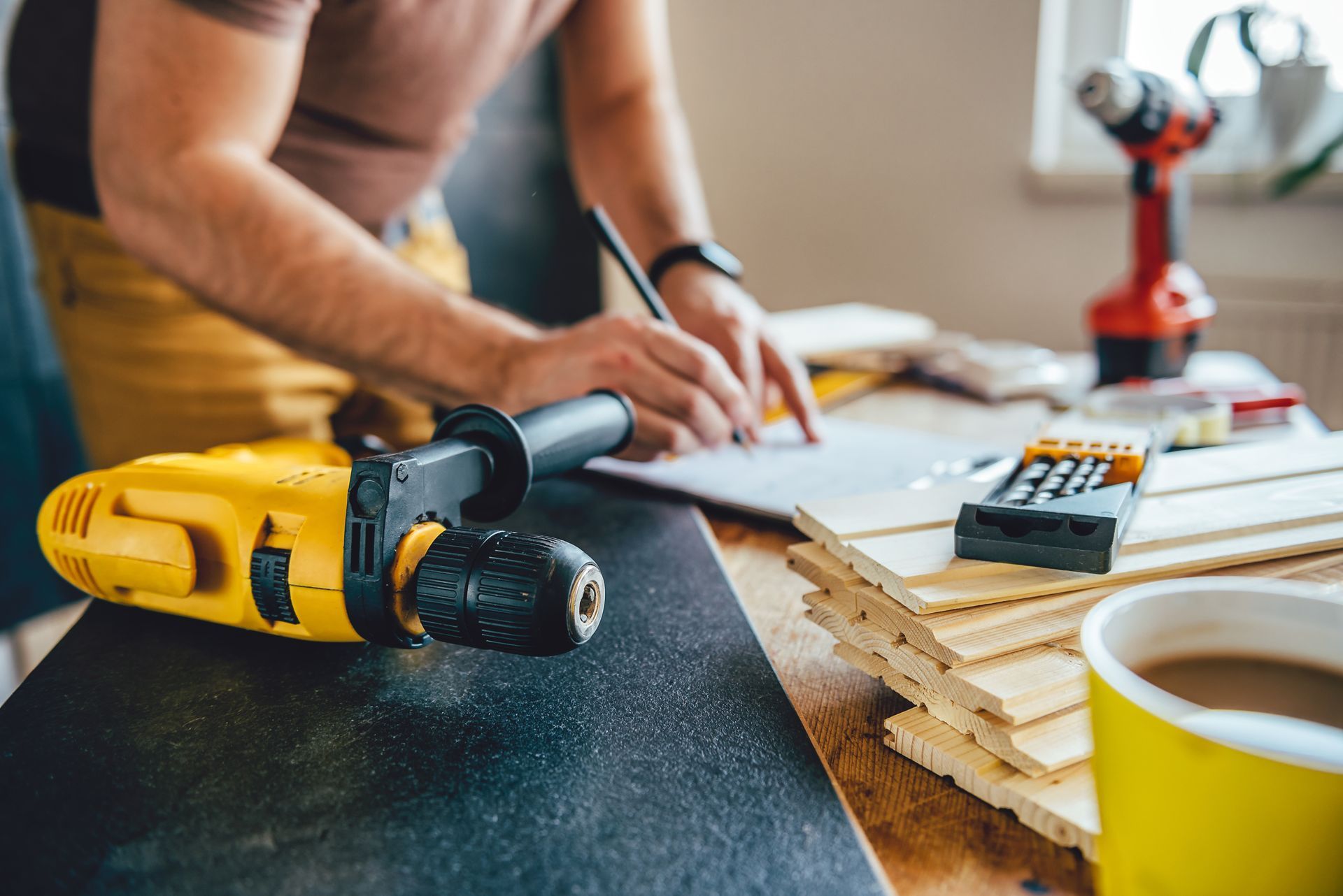 Person using a pencil to write on paper, surrounded by woodworking tools and materials.