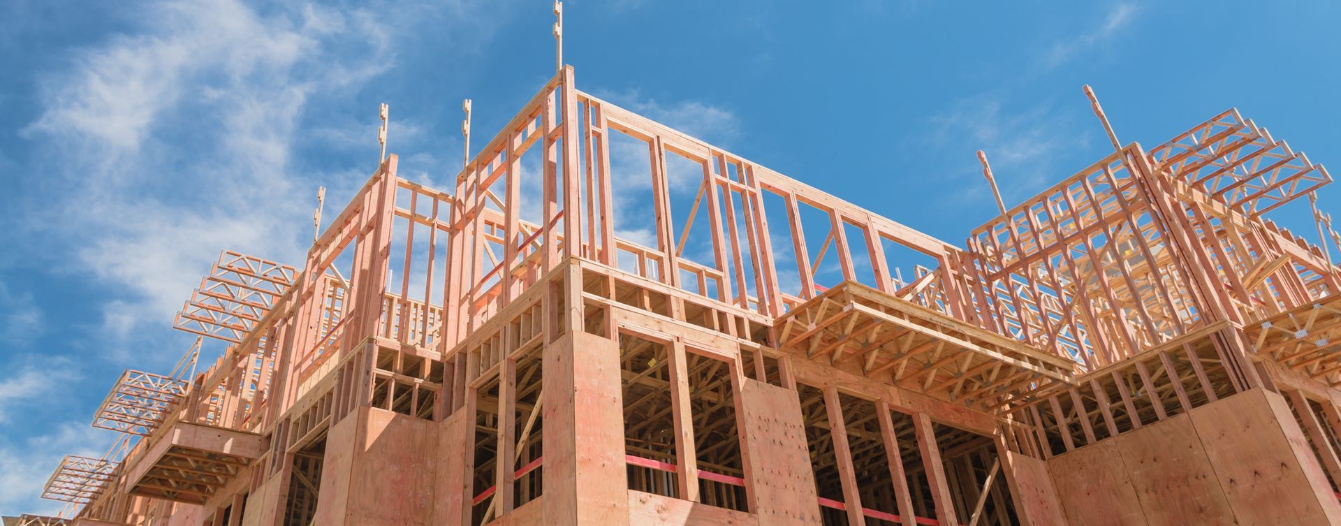 Wooden frame of a building under construction against a blue sky with scattered clouds.