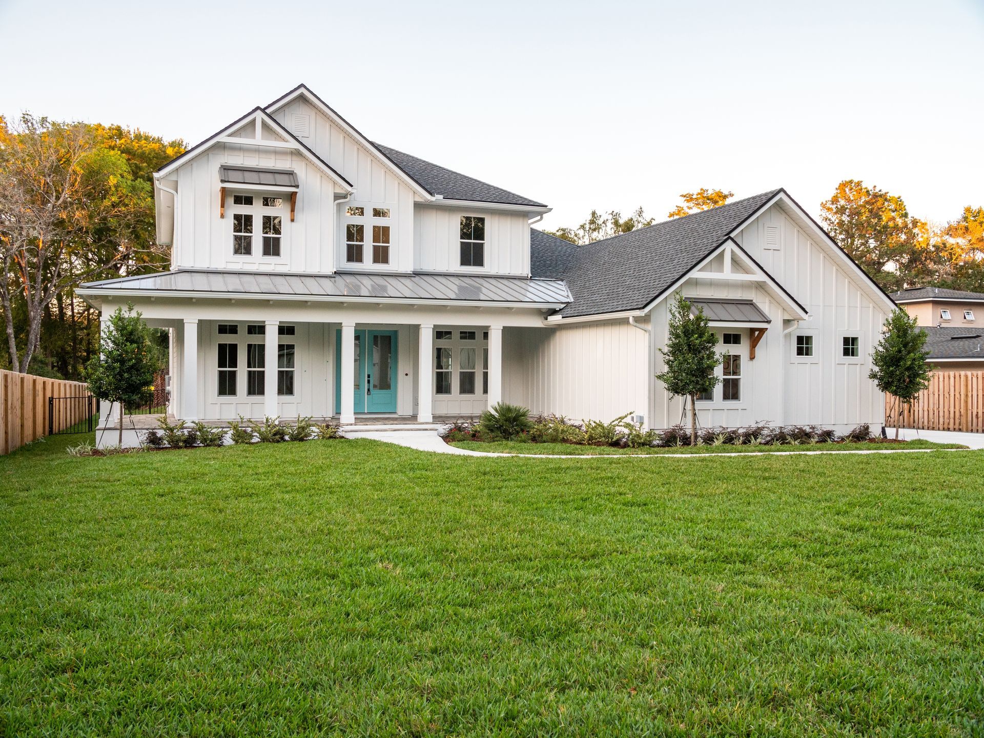 White farmhouse with turquoise door, green lawn, and wooden fence.