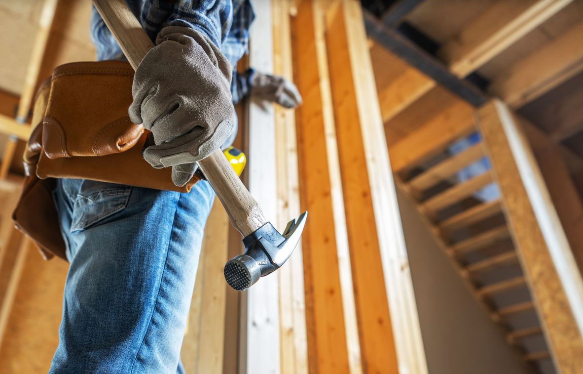Carpenter with hammer and tool belt at a construction site, framed wood interior.