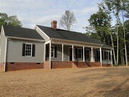 A light gray ranch-style house with a brick foundation and a porch. Black shutters and a dark roof.