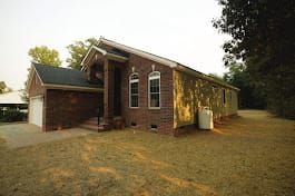 Brick house with a garage, arched windows, and a propane tank. Overgrown lawn.