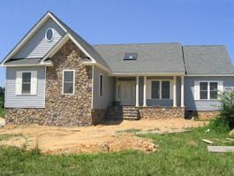 Gray house with stone accents and blue siding; front yard under construction.