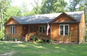 Brown wooden house with front porch, windows, and American flag on a grassy lawn.