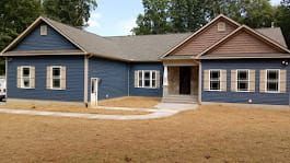 Blue house with brown roof and beige shutters, on dry grass.