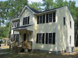 Two-story house with yellow siding, black shutters, and wooden porch.