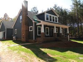 Two-story house with dark gray siding, white trim, and a brick chimney, with a porch and attached garage.