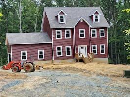 Two-story red house under construction with a tractor in the yard.