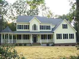 Yellow two-story house with black shutters and porch, set in a yard with trees.