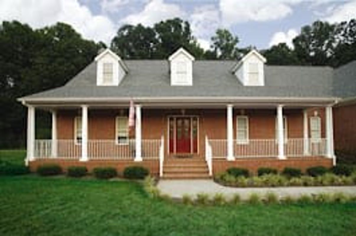 Brick house with porch, white pillars, three dormers, and green lawn.
