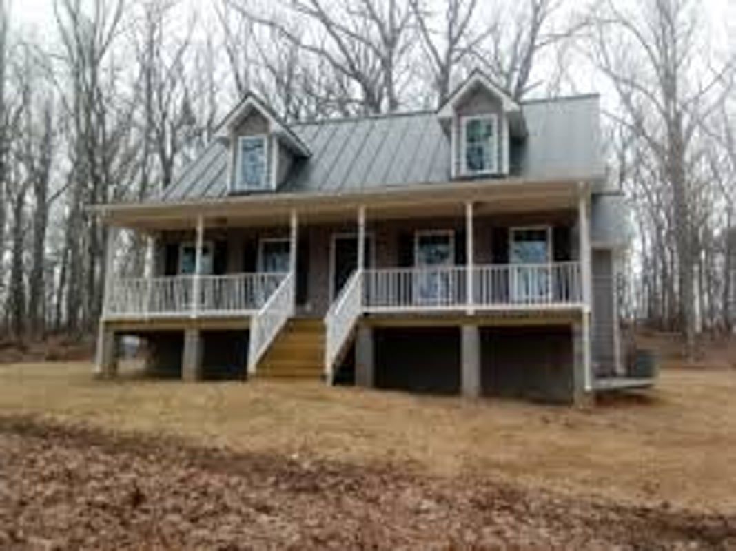 Cottage-style house with dormers, porch, and a raised foundation, set among bare trees.