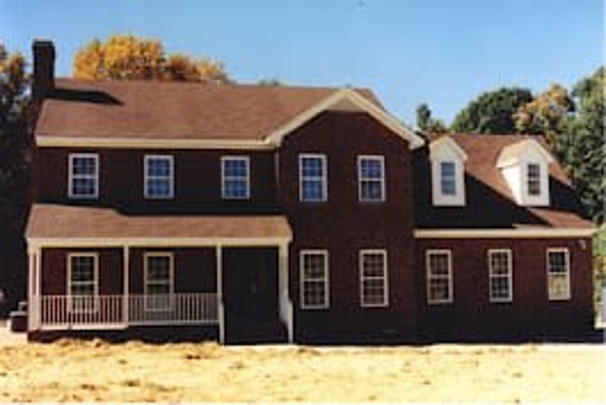 Two-story brick house with a porch and dormers, brown roof, set on a construction site.