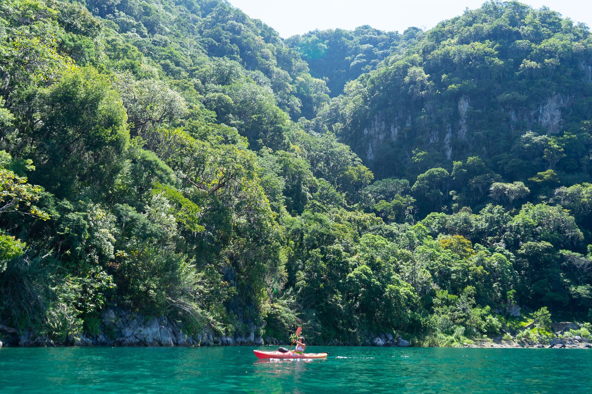 A person in a red kayak in a lake with mountains in the background