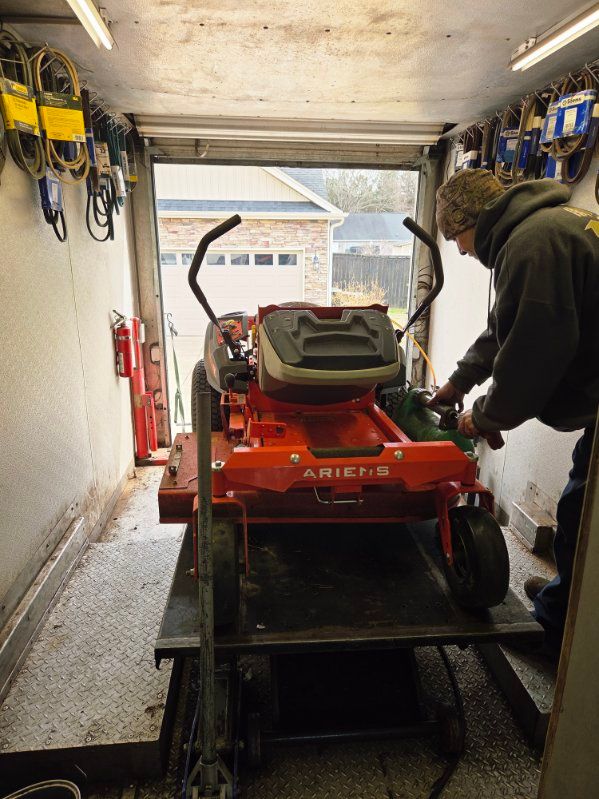 Orange snowblower inside a trailer while a person adjusts it near the open rear door.
