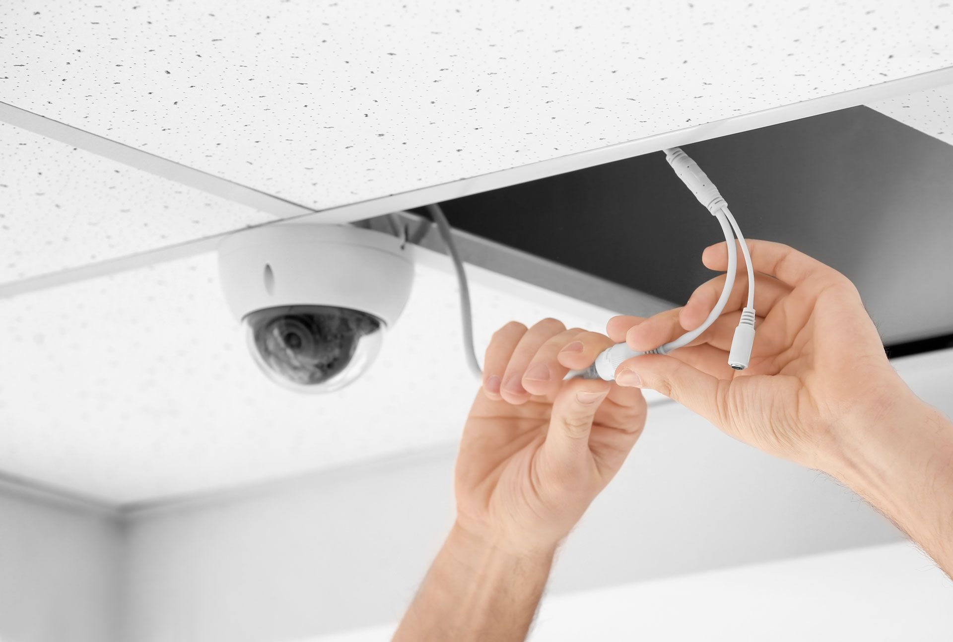 A person is installing a security camera on the ceiling.
