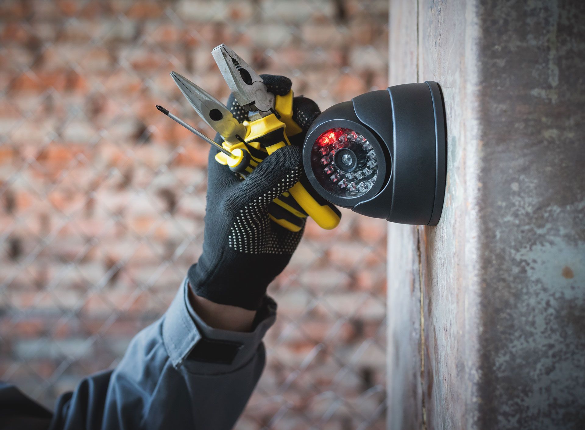 A person is installing a security camera on a brick wall.