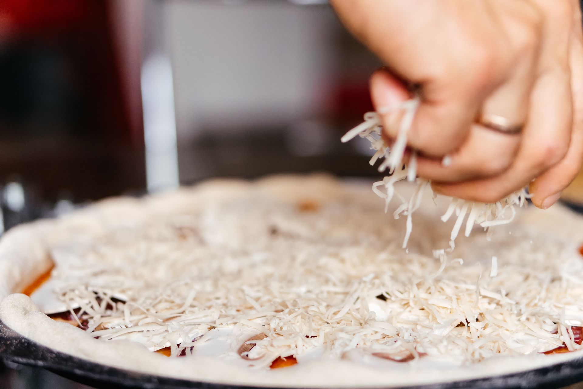 Hand adding shredded cheese to a customized pizza before baking.