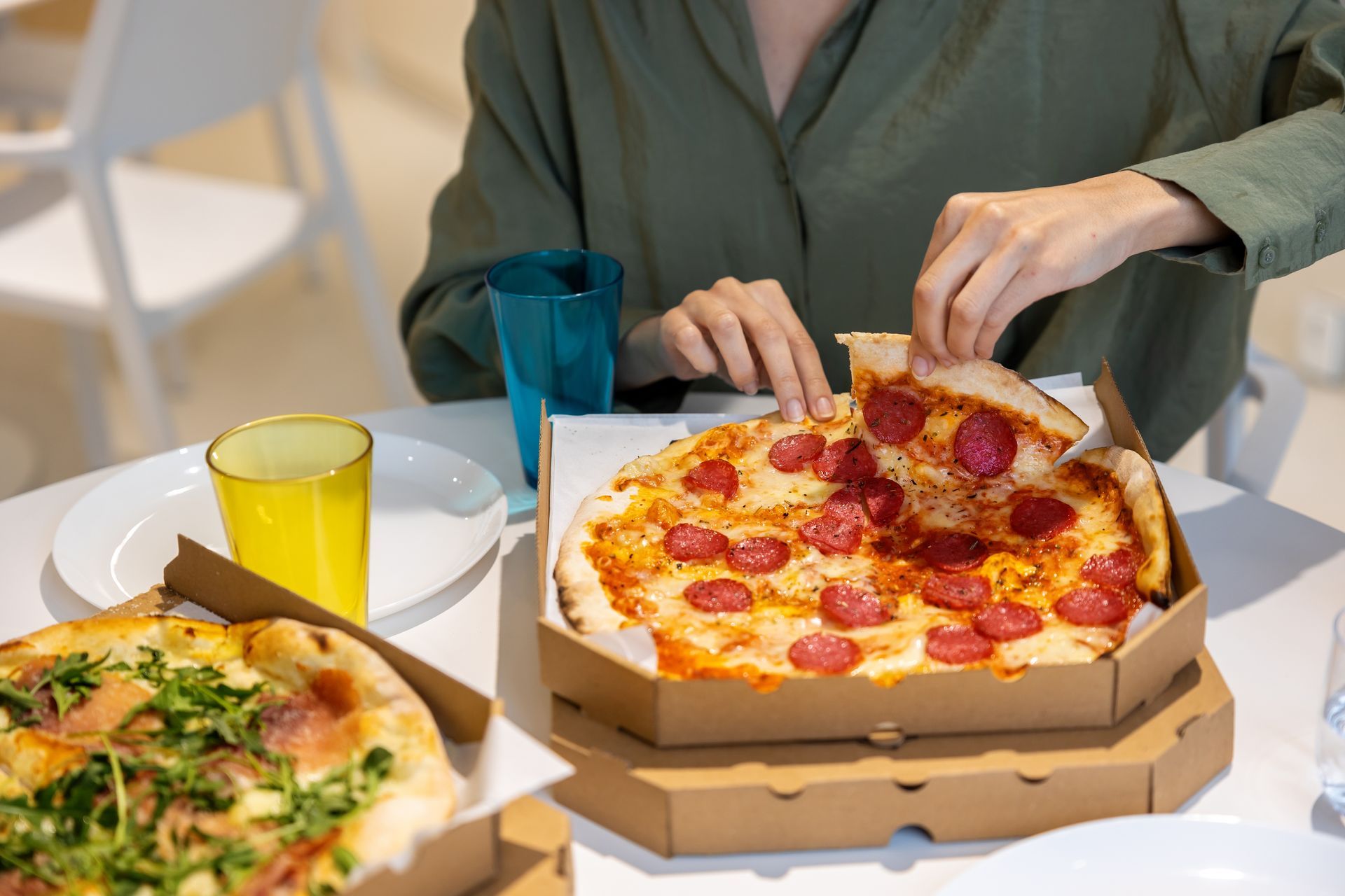 Person with pizza in a box and a red drink on a wooden table. Person with pizza in a box and a red drink on a wooden table.