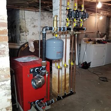 A red boiler is sitting in a basement next to a brick wall.