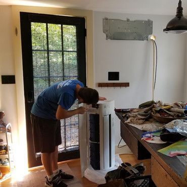 A man in a blue shirt is working on an air conditioner in a living room.