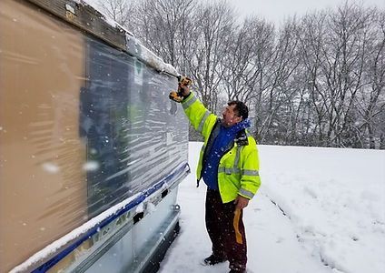 A man in a yellow jacket is cleaning a window in the snow.