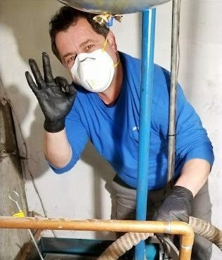 A man wearing a mask and gloves is standing next to a pipe.