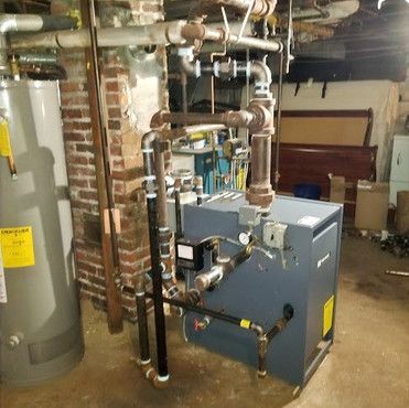 A boiler is sitting in a basement next to a water heater.