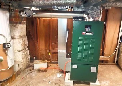 A green boiler is sitting in a basement next to a wooden door.