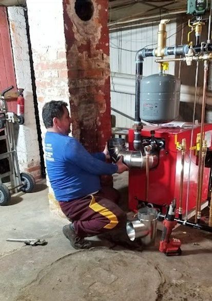 A man is working on a red boiler in a basement.