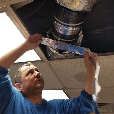 A man in a blue shirt is working on a duct