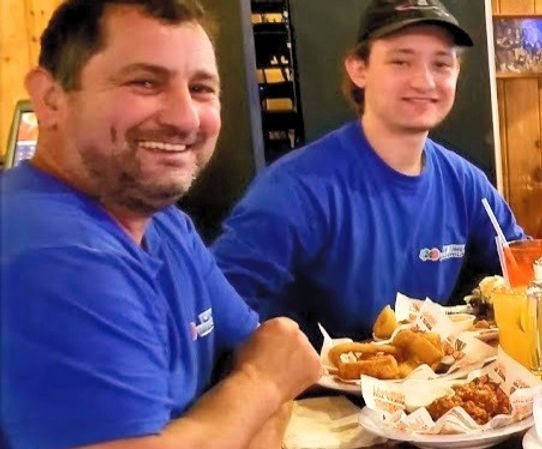 Two men in blue shirts are sitting at a table with plates of food