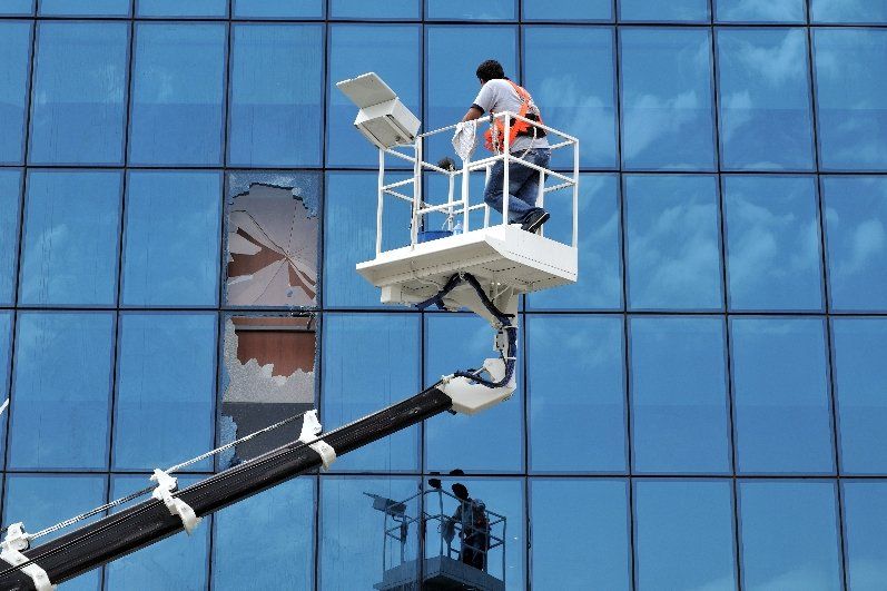 man on a lift to repair large broken window on the side of a tall office building