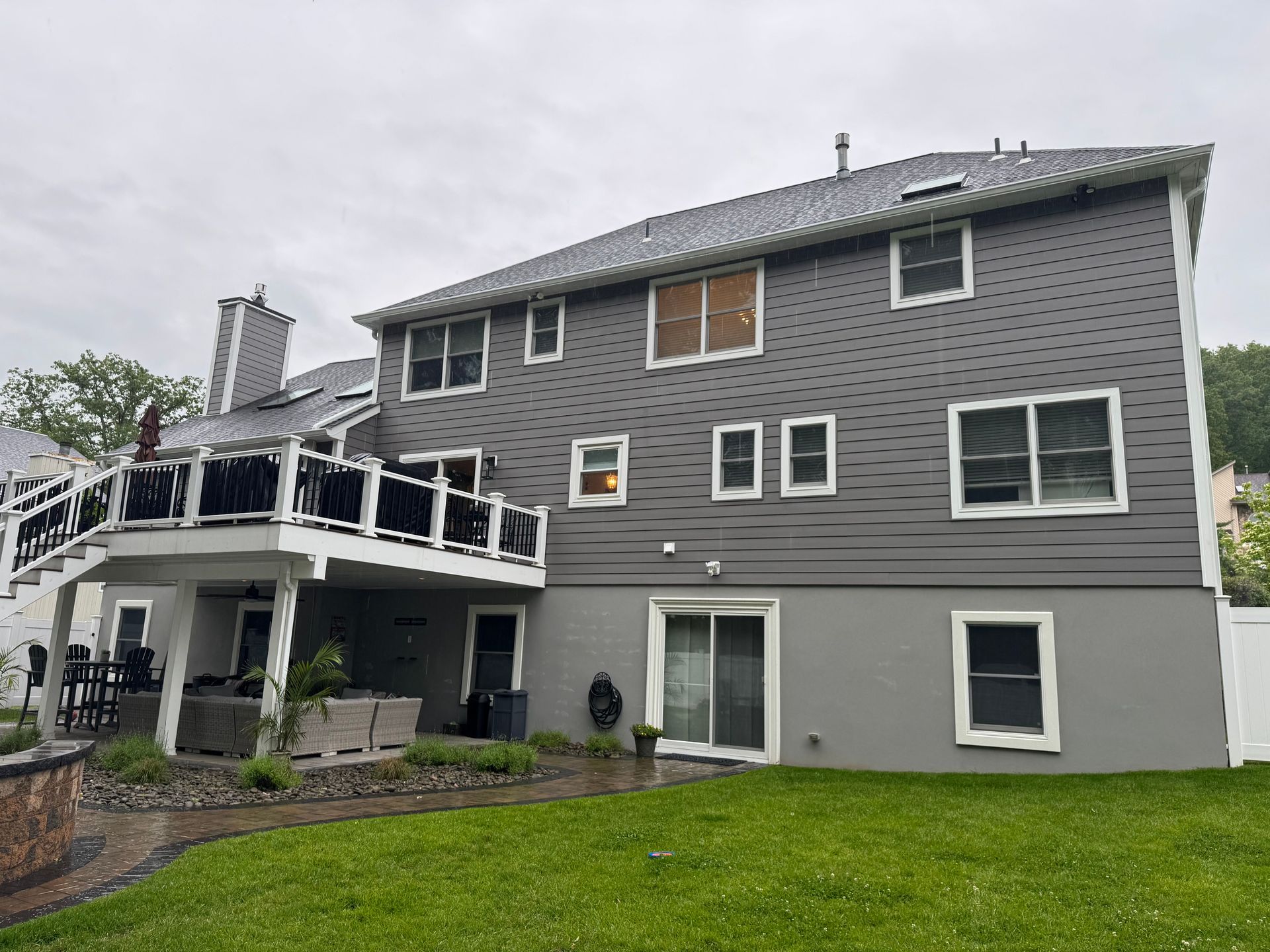 A two-story house exterior with grey siding and a large white deck overlooking a grassy backyard.